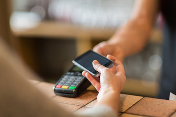hands with payment terminal and smartphone at bar