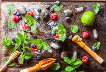 Refreshing mint cocktail mojito with lime and berries , cold drink or beverage with ice and cold cocktail stones on black old metal background, top view