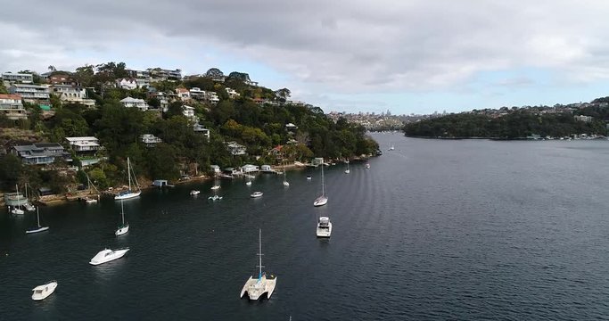 Dense residential area with houses and moored yachts along shores of Sydney Harbour in Seaforth suburb flying along wateredge.