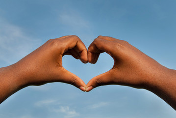 Black hands in heart shape with blue sky background