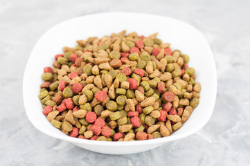 Lot of dry coloured cat food in white ceramic bowl on old gray concrete floor