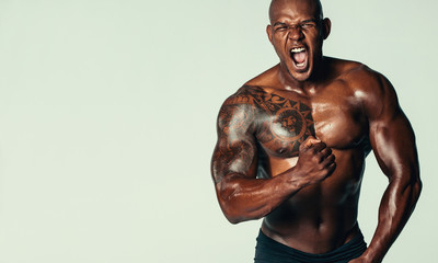 Aggressive bodybuilder screaming against grey background