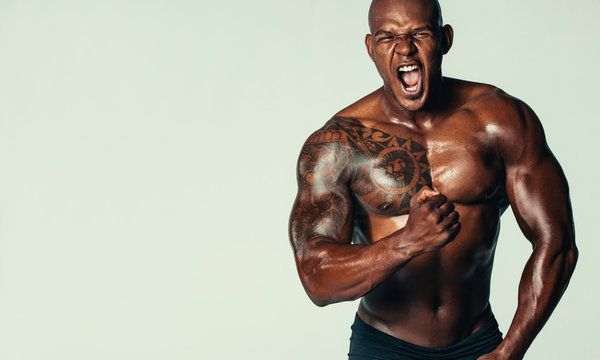Aggressive bodybuilder screaming against grey background
