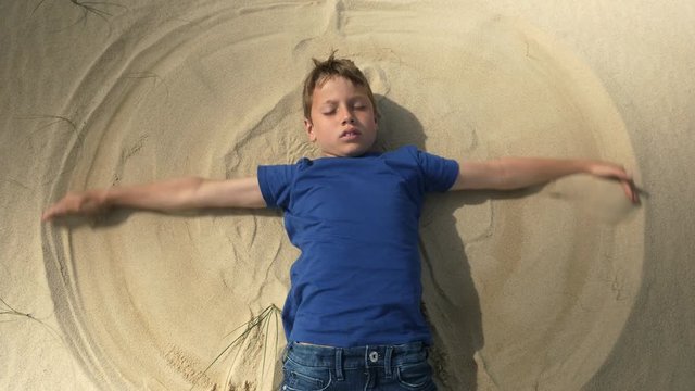 Dreamy boy doing a sand angel at the beach