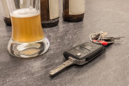 Bier in einem Glas und Autoschlüssel auf dem Tisch und leere Bierflaschen im Hintergrund