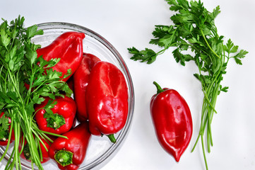 Raw red organic peppers with  bunch of aromatic green spice parsley in a glass bowl ready to cook with isolated on white