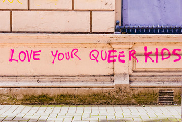 Pink graffiti on a wall saying "Love your queer kids"