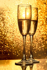 Two champagne glasses of toasting on the glossy table surface against gold bokeh background.