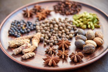 Aromatic spices on a dark plate - star anise, fragrant pepper, calamus root, cinnamon, nutmeg close up on brown background. Spices texture background. Side view