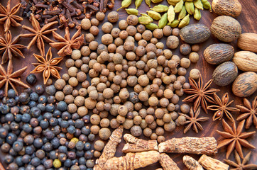 Aromatic spices on a dark brown plate - star anise, fragrant pepper, calamus root, cinnamon, nutmeg, juniper berries close up. Spices texture background. Top view