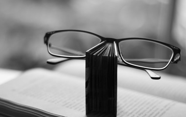 Black & white style of congratulations on Teachers Day. A book holds glasses, as if on a nose of person or a mustache on a background of another open book.