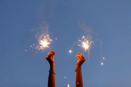 Woman's hand holding sparkler to the sky at twilight
