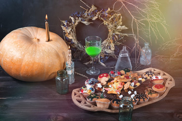 Pumpkin, candle, green liquid in a glass, sweets, cookies, jars, dry twigs and leaves on a table