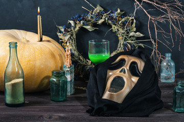 Scary mask for Halloween, green liquid in a glass, pumpkin, powder, candles, dry twigs and leaves