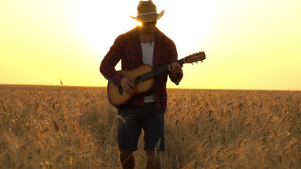 young guy walks the golden wheat field in the rays of the sunset and plays the guitar.