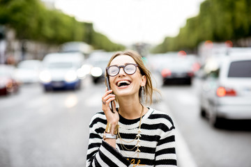 Fototapeta premium Young and happy woman talking with smart phone standing outdoors on the street with traffic in Paris