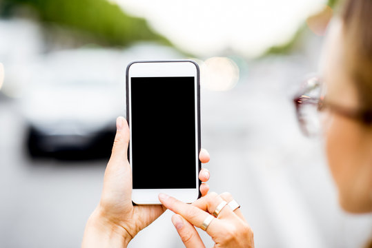 Mockup image of the woman holding a smart phone outdoors on the street background