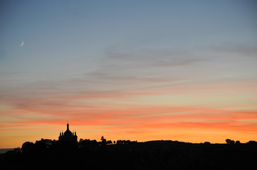 Beautiful sunset - silhouette of the church, trees, forest and young moon in the corner of the photo