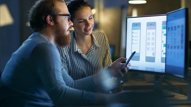 Handsome Male and Beautiful Female Mobile Application Designers Test and Discuss New App Features. They Work on a Personal Computer with Two Displays, in a Creative Office Space.
