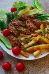 Chicken ribs in honey sauce with French fries and vegetables.