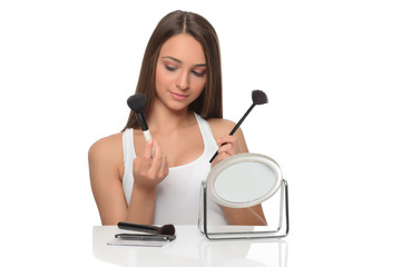  A young woman applying makeup on her face with a brush