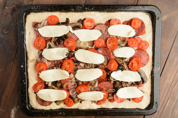 Unready homemade pizza on baking pan over wooden background