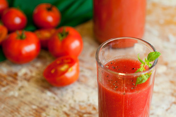 Glass and bottle of tomato juice with vegetables and green napkin on wooden background