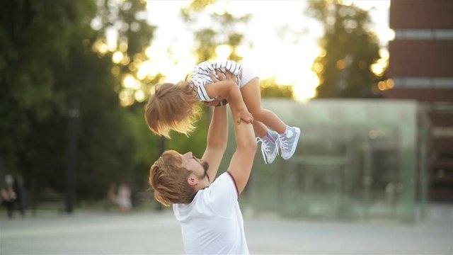 Young Husband Lifts Daughter Over His Head. Father Plays with Little Cute Girl, Family Enjoys Playing Outdoors.
