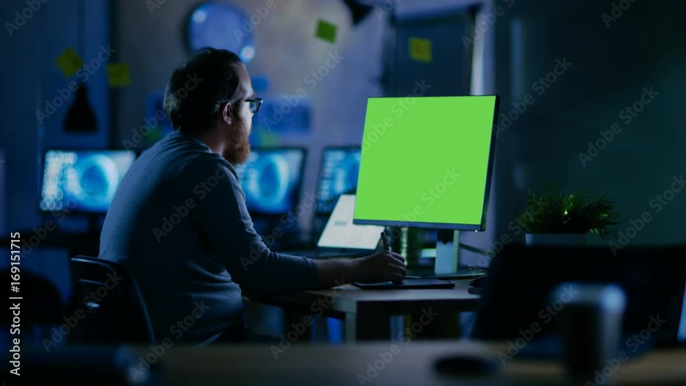 Poster Creative Bearded Man Works on a Personal Computer with Isolated Mock-up Green Screen. He Works Alone in the Office Late at Night. Shot on RED EPIC-W 8K Helium Cinema Camera.