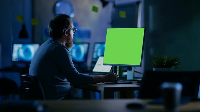 Creative Bearded Man Works on a Personal Computer with Isolated Mock-up Green Screen. He Works Alone in the Office Late at Night. Shot on RED EPIC-W 8K Helium Cinema Camera.