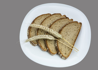 Bread and cereal spikes on a white plate. Four slices of bread with decorative dry barley. Isolated on gray background.