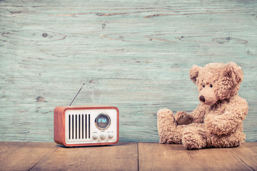 Retro Teddy Bear toy and fm radio receiver front textured wooden wall background. Listening music concept. Vintage old instagram style filtered photo