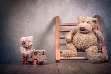 Two retro Teddy Bear toys family: parent with baby driving on wooden vehicle front concrete wall background. Parenthood concept. Vintage instagram old style filtered photo