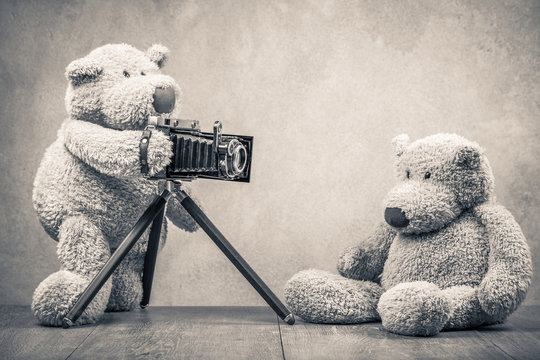 Teddy Bear toy photographer with old retro outdated film camera making photo shoot of model sitting on wooden floor. Vintage style sepia photo