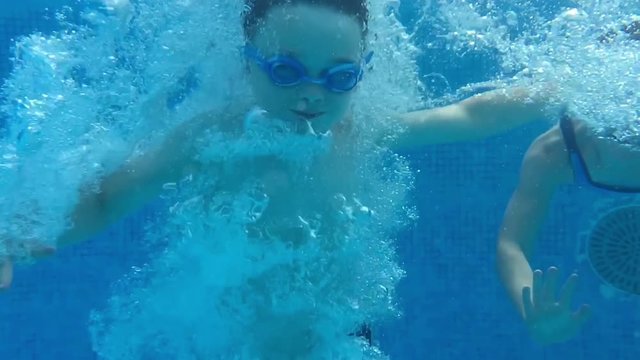 Children having fun in the pool on a hot summers day. Amazing slow motion bubbles of child jumps into pool