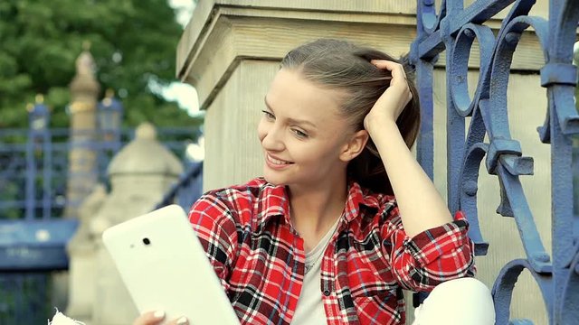 Pretty girl in checked shirt wearing rollerblades and doing selfies on tablet, steadycam shot
