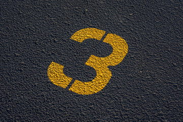 stenciled number 3 three in yellow paint on blacktop in parking lot - for use as background