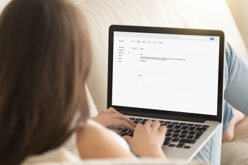 Woman typing electronic message to partner on laptop while working from home, writing commercial...