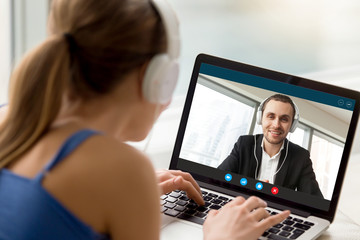 Man and woman in headphones communicating online by video call, looking at full screen...