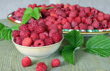 Bowl and tray natural ripe berries and green leaves on a wooden table