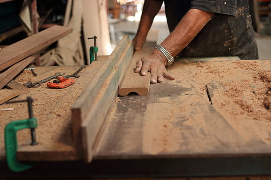 Piece of wooden board is being shaved on a router table by hands of senior carpenter in carpentry workshop.Selective focus and shallow depth of field.
