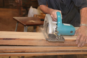 Electric circular saw is being cut a wood board by workers in woodwork shop.