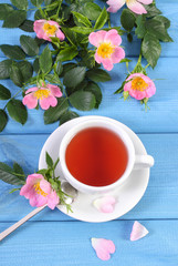Cup of tea and wild rose flower on boards