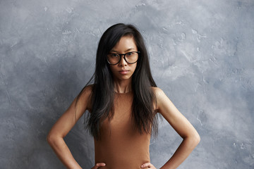 Studio shot of annoyed irritated brunette girl of Asian appearance wearing eyeglasses posing at...