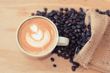 Coffee cappuccino in white cup and coffee beans on the wooden floor