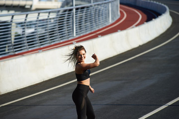 Outdoor summer shot of happy woman runner sprinting towards success on run path. Attractive cheerful female sprinter doing fast sprint for competition at stadium. Goal, winning and achievement