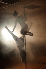 Two young girls doing acrobatic tricks with a pole
