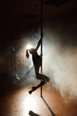 Naklejka na ściany i meble Young sexy woman exercise pole dance on a dark background