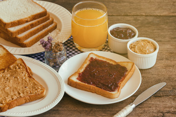 Toast bread with homemade strawberry jam and peanut butter served with orange juice. Homemade toast bread with jam and peanut butter on wood table for breakfast. Delicious toast bread ready to served.