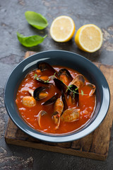 Seafood soup with mussels and vongole shells served in a dark grey plate, studio shot